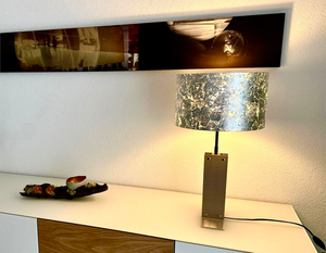 Handgefertigte Tischleuchte aus Edelstahl nach Mass mit Lampenschirm aus Schlagmetall in Silberoptik auf einem stilvollen Sideboard