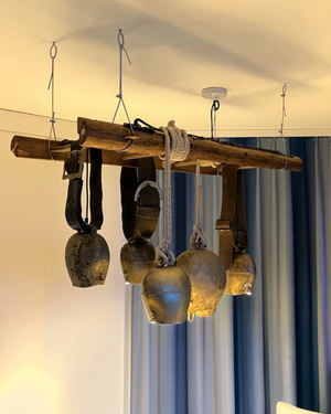 Massgefertigte Hängeleuchte aus alten Glocken und einer Holzleiter in einer Ferienwohnung in den Schweizer Alpen